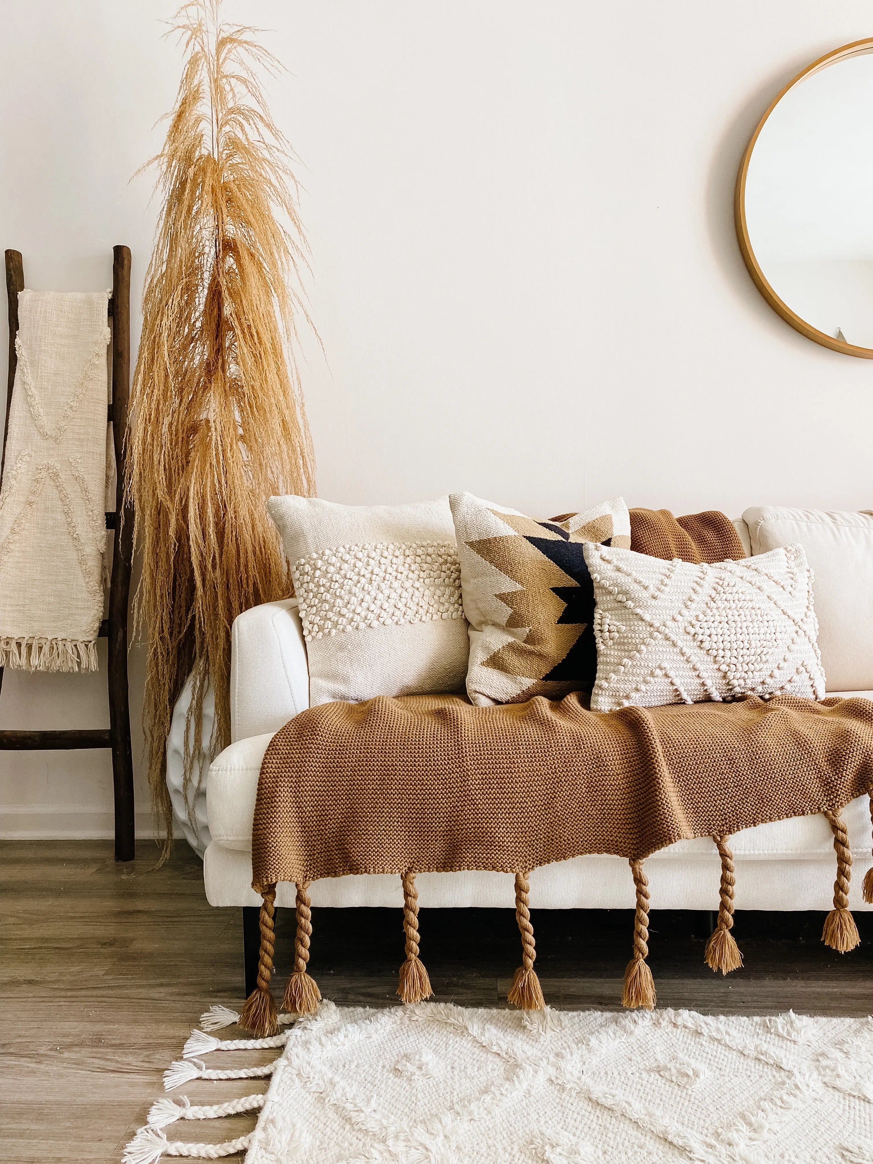 Cozy farmhouse living room with textured throw pillows, knit blanket, dried pampas grass, and round mirror decor