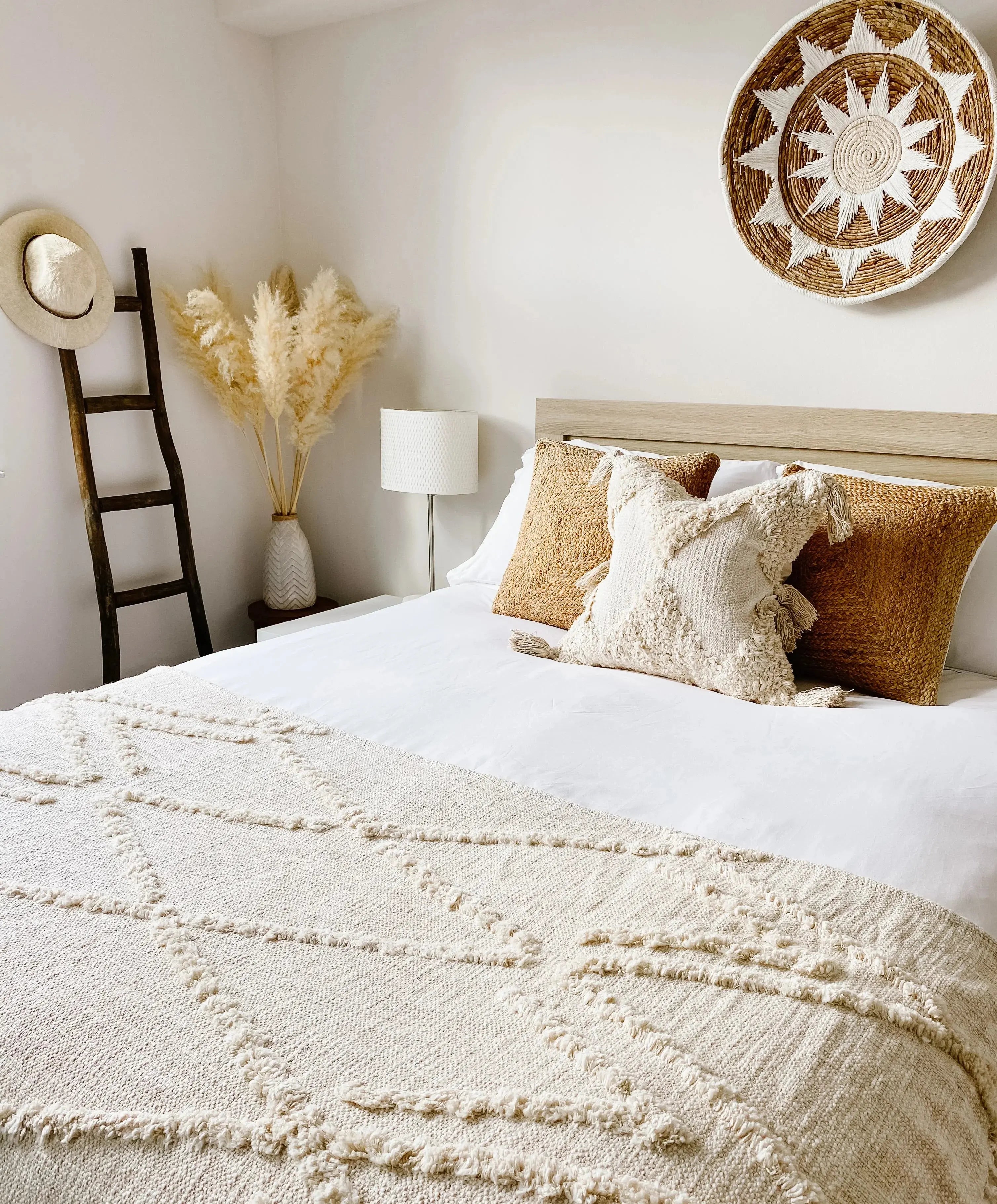 Cozy farmhouse bedroom with textured knit blanket, woven pillows, and sunburst wall decor