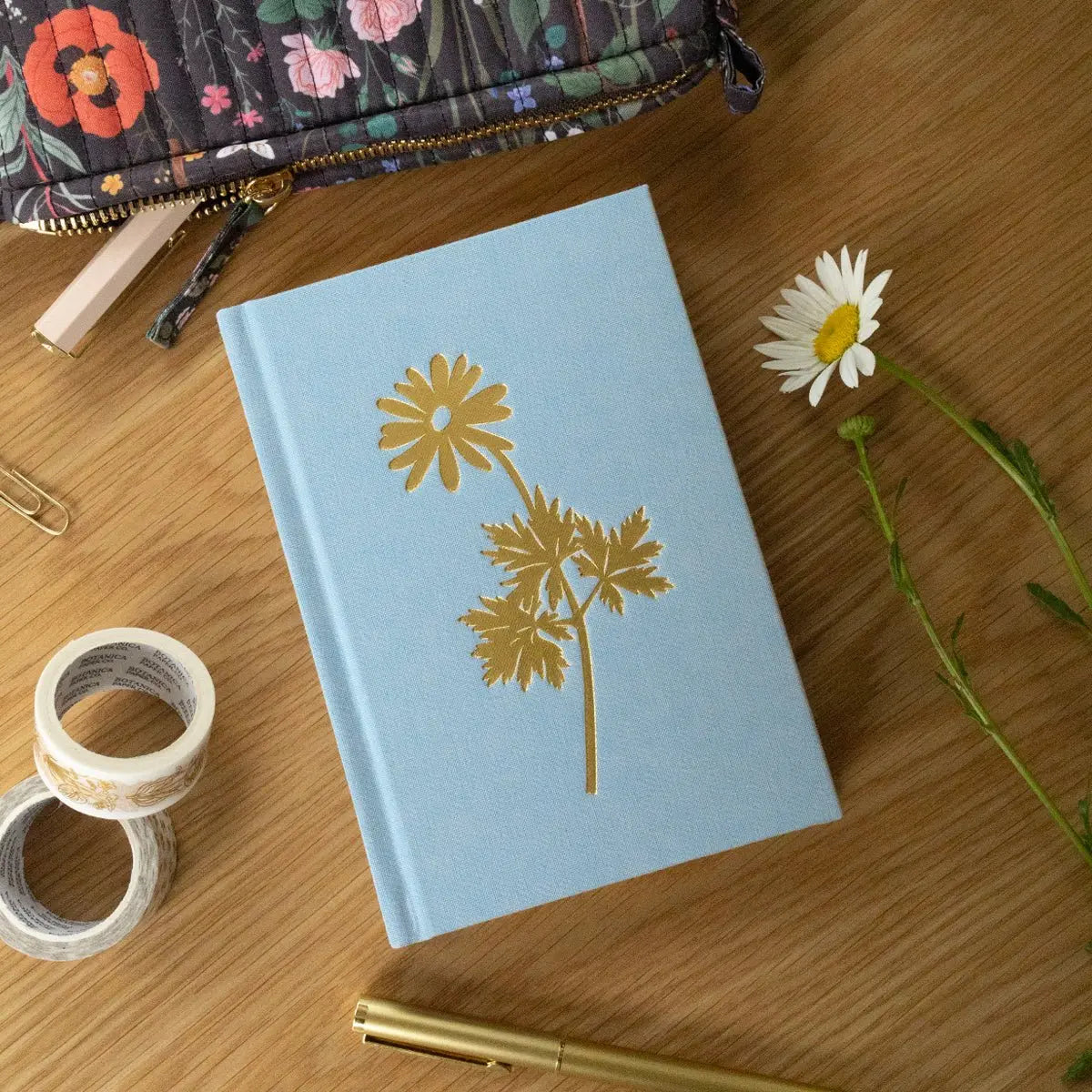 Light blue notebook with floral design on a wooden surface with a pen and tape.