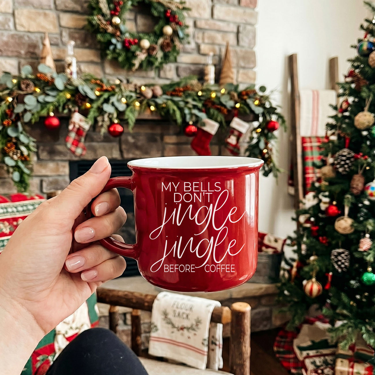 Person holding a red mug with Christmas-themed text in a festive living room.