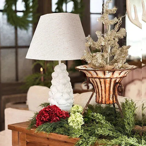 Cozy farmhouse table decor with white textured lamp, frosted tree, red & green flowers, rustic planter