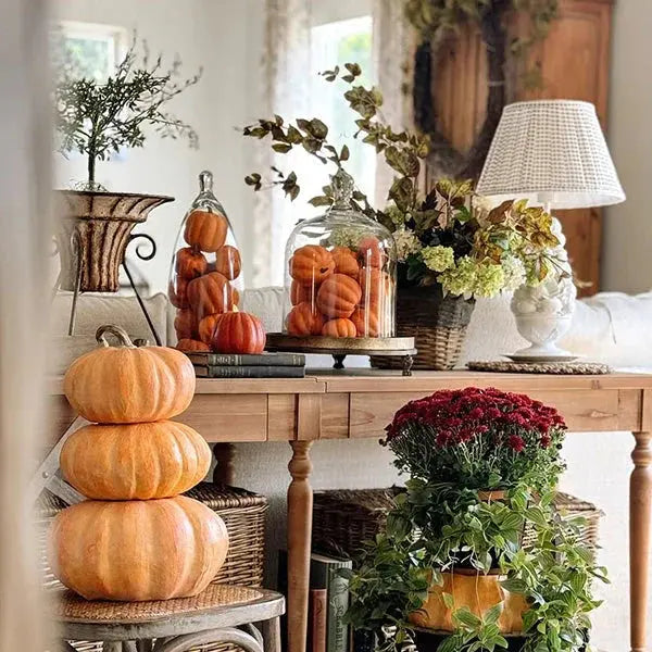 Cozy farmhouse fall decor with stacked pumpkins, glass cloches, and autumn flowers on wooden console table