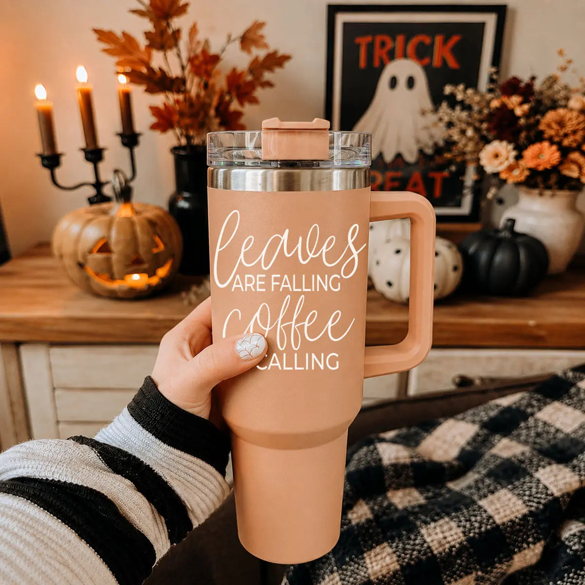 Person holding a 'Sweater weather' travel mug with Halloween decorations in the background