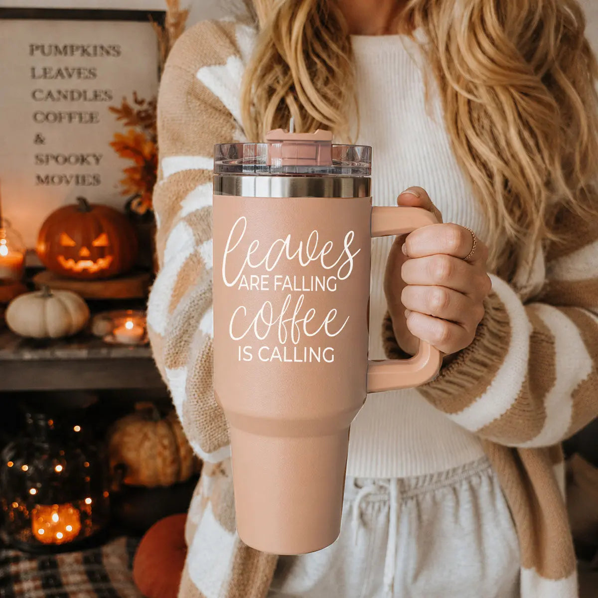 Person holding a 'sweater weather' mug with Halloween decorations in the background
