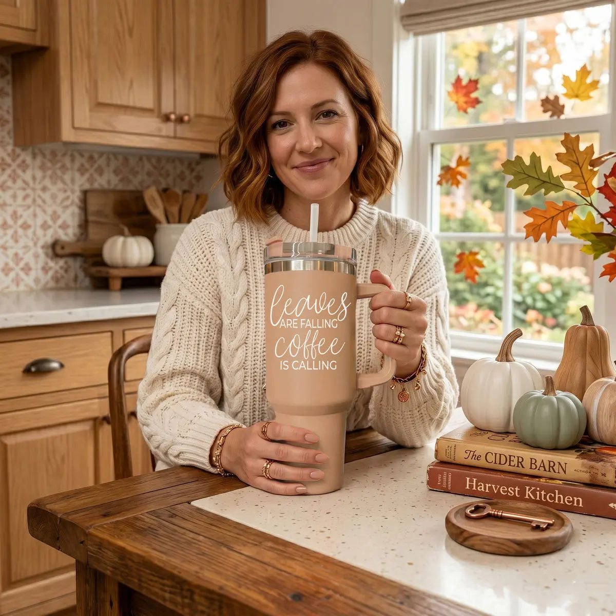 Woman holding a 'Sweeter Weather' tumbler in a kitchen with autumn decorations.