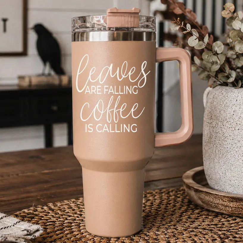 Beige travel mug with 'Leaves are falling, coffee is calling' text on a wooden table.