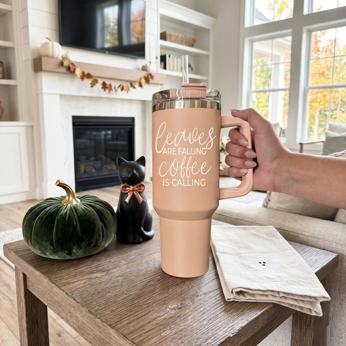 Person holding a tan mug with 'Sweater weather' text in a cozy living room.
