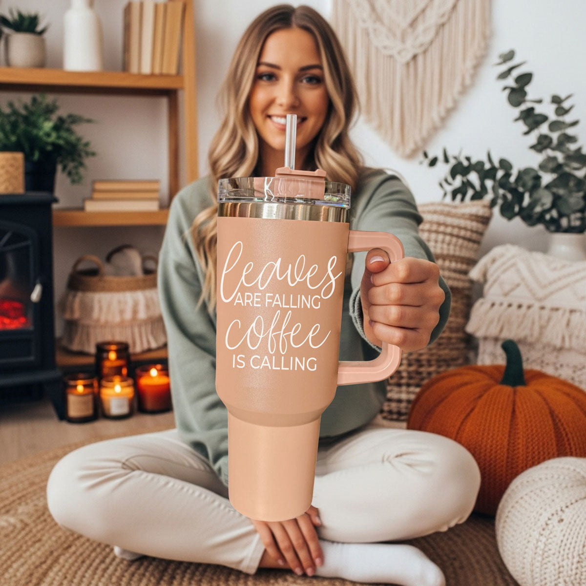 Woman holding a pink insulated mug with 'Sweeter Weather' text in a cozy living room.