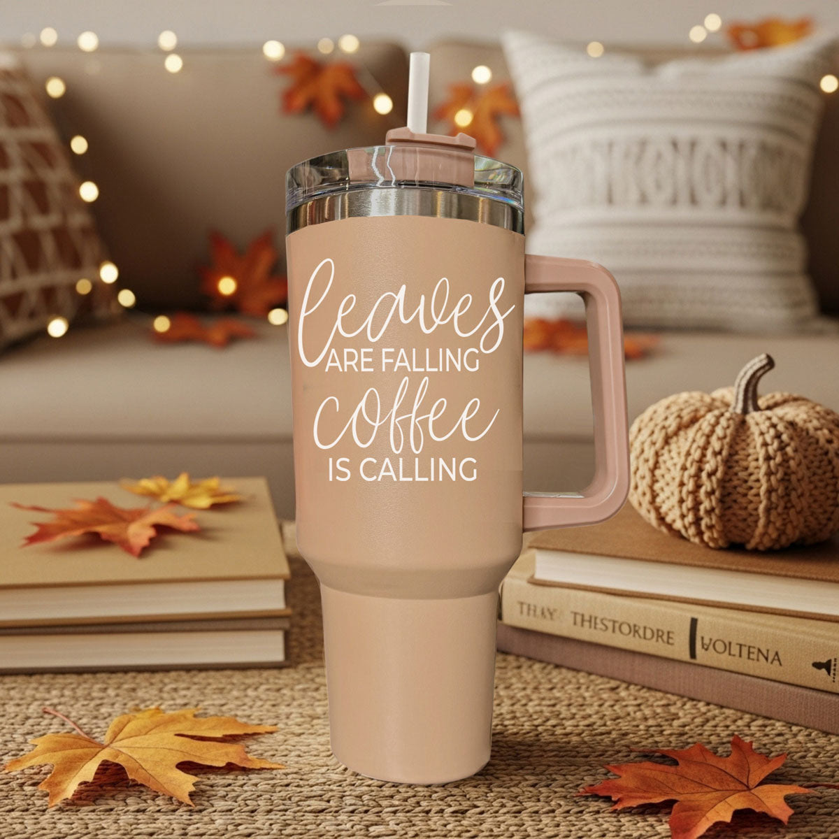 Pink travel mug with 'leaves are falling coffee is calling' text, surrounded by autumn decor.