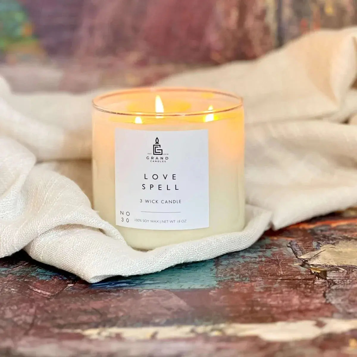 Love Spell 3-wick soy candle glowing on rustic surface, cozy farmhouse decor