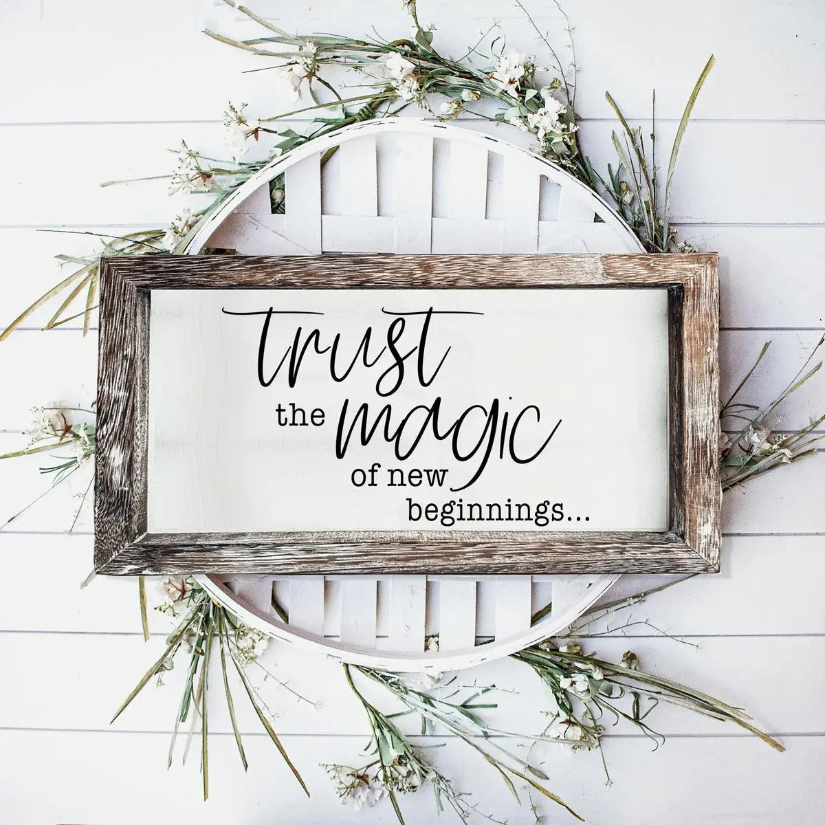 Wooden sign with 'Trust the magic of new beginnings' text on a white background with greenery.