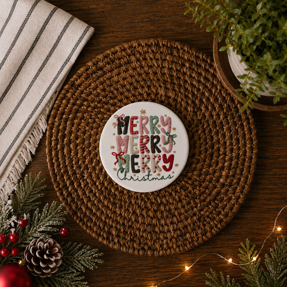 Round woven placemat with a 'Merry Christmas' coaster on a wooden surface with holiday decorations.