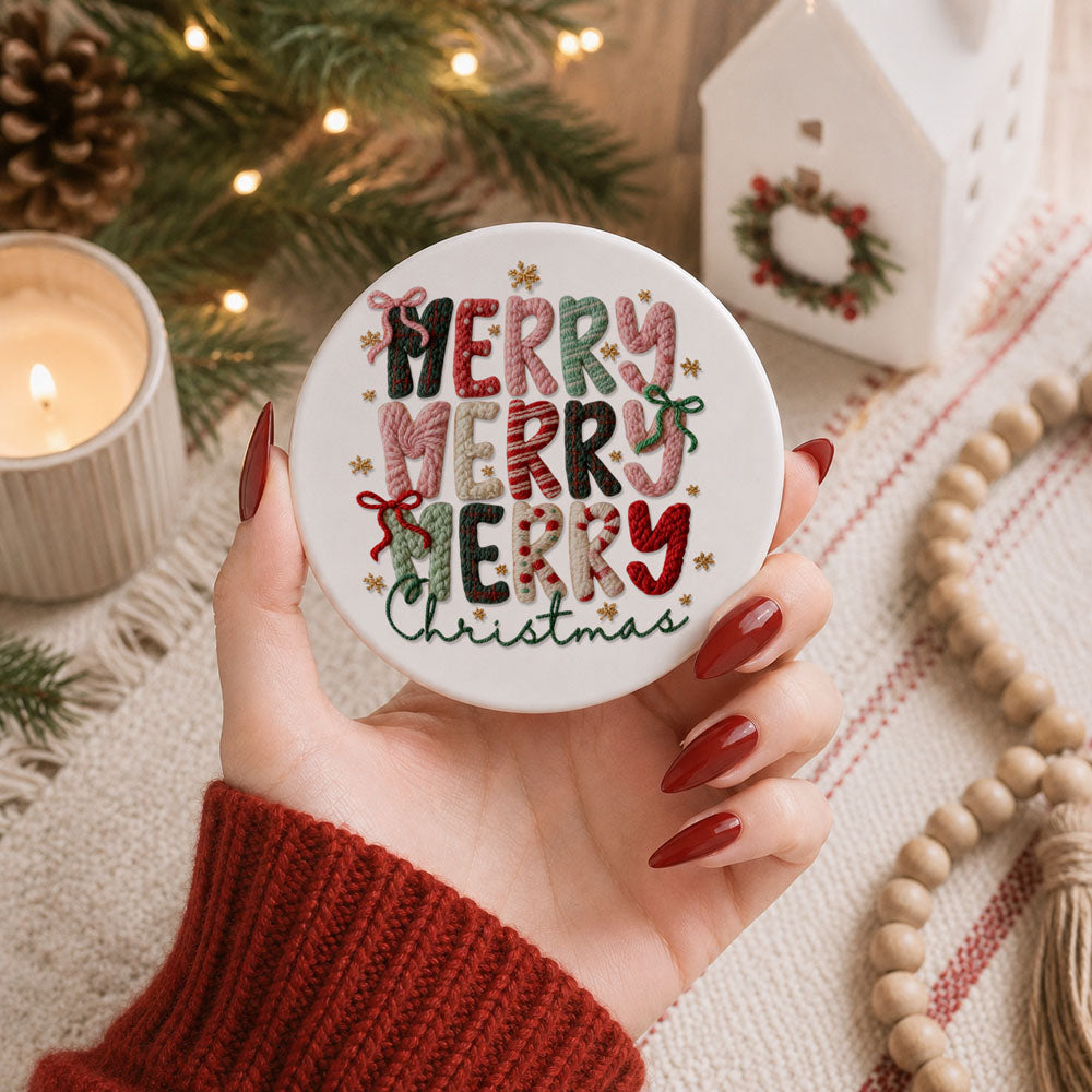 Hand holding a round ornament with 'Merry Christmas' text, surrounded by festive decor.