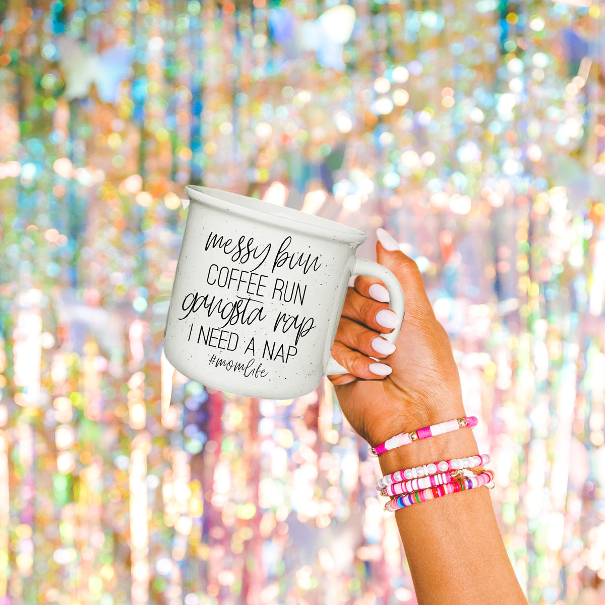 Hand holding a mug with 'mom of sassholes' text against a colorful, blurred background