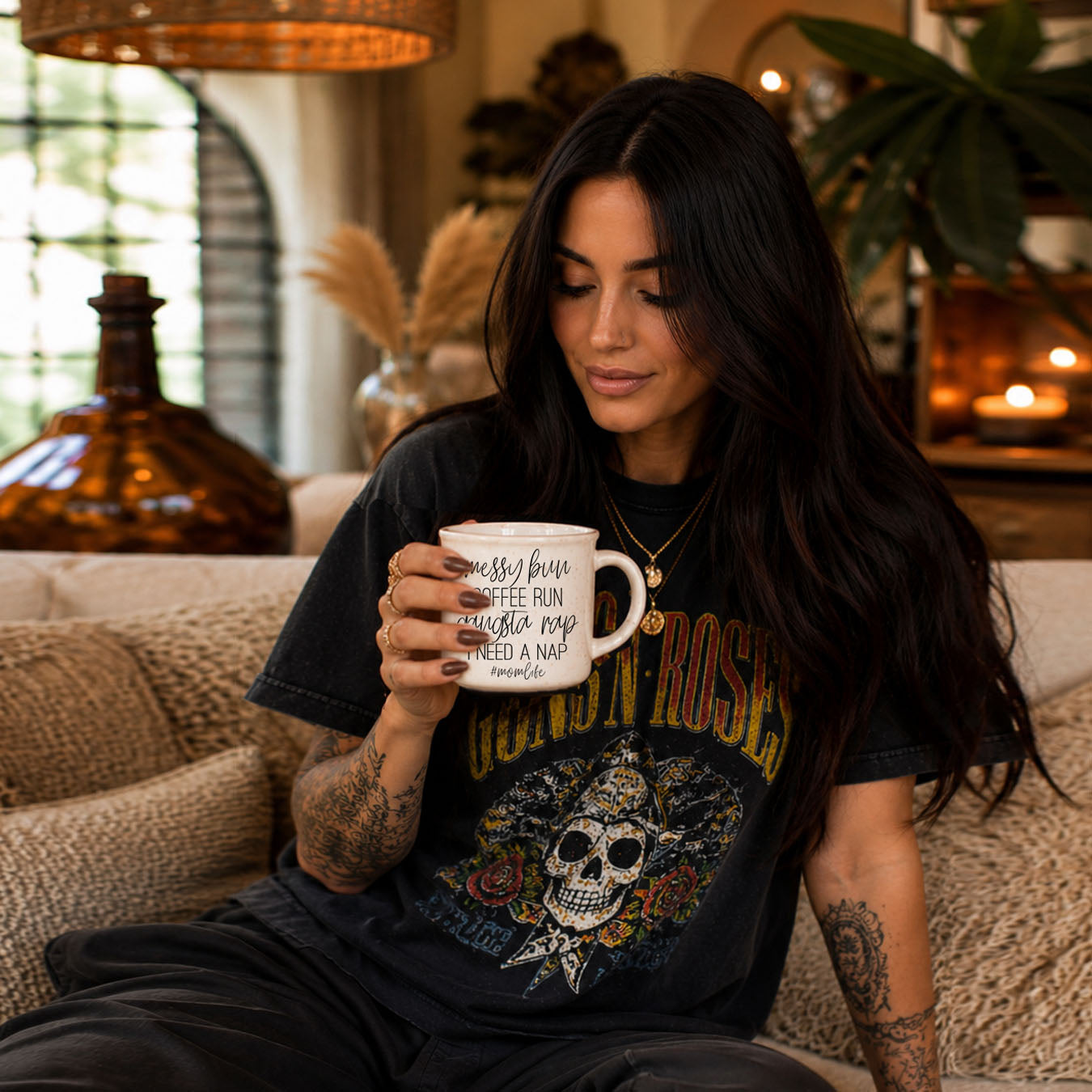 Woman holding a mug with text, wearing a graphic t-shirt, sitting on a couch in a cozy room.