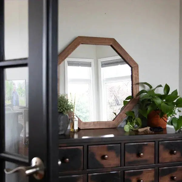 Rustic octagon wood mirror on dark farmhouse dresser with green plant, cozy cottage decor