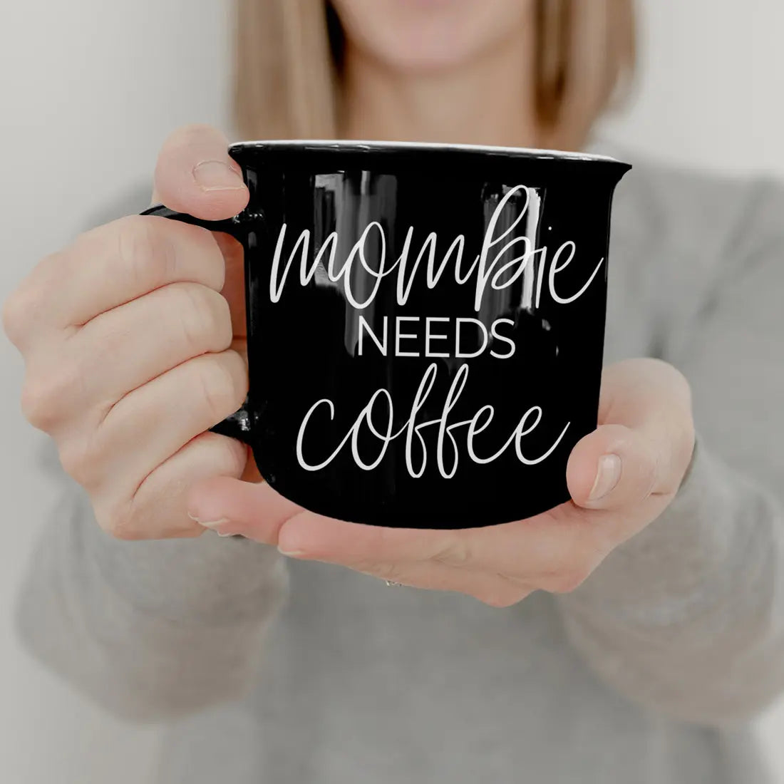 Person holding a black mug with 'mommy needs coffee' text.