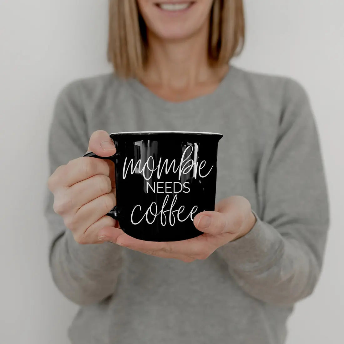 Person holding a black mug with 'mommy needs coffee' text against a plain background