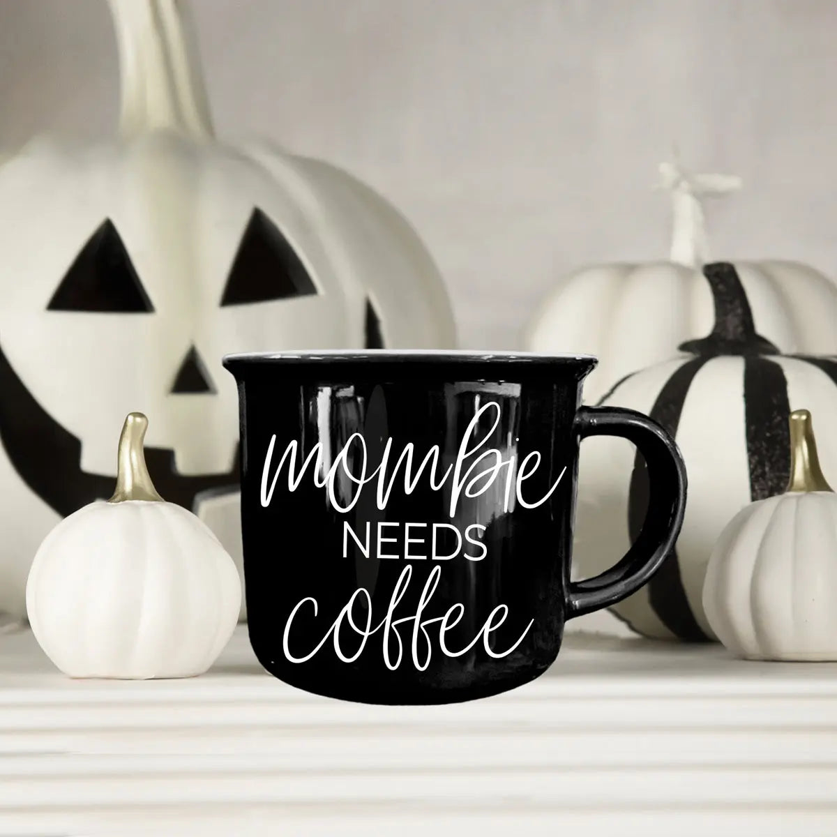 Black mug with 'mommy needs coffee' text in front of Halloween pumpkins.