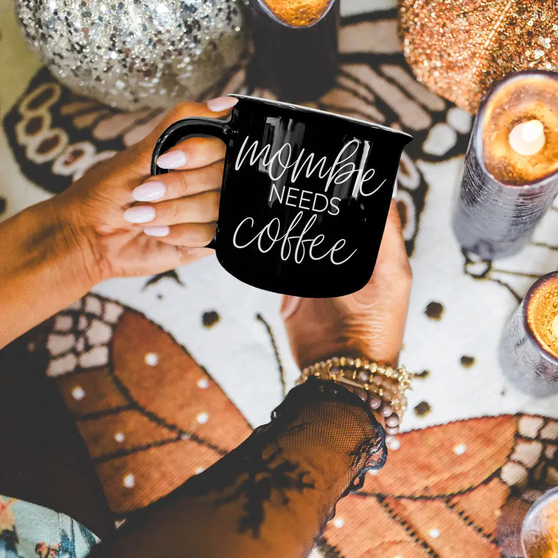 Person holding a black mug with 'Mommy Needs Coffee' text on a decorative surface.