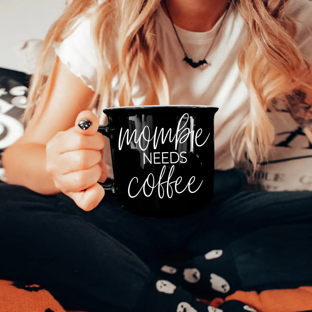 Person holding a black mug with 'mommy needs coffee' text, sitting on a couch.