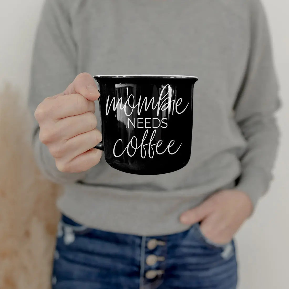 Person holding a black mug with 'mommy needs coffee' text against a neutral background
