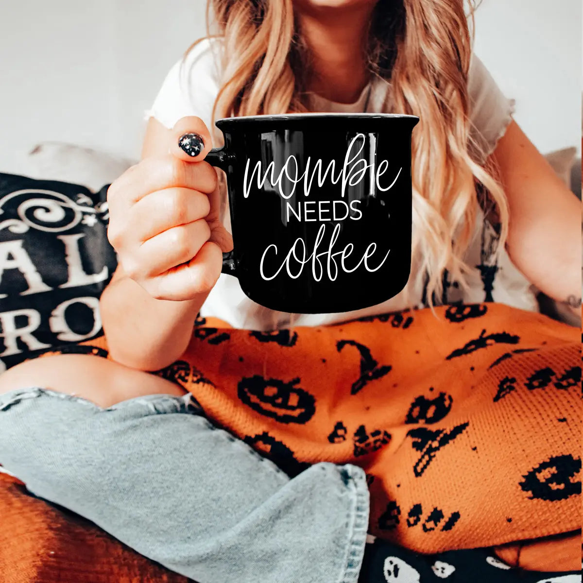 Person holding a mug with 'mom life needs coffee' text, wearing a Halloween-themed blanket and shirt.