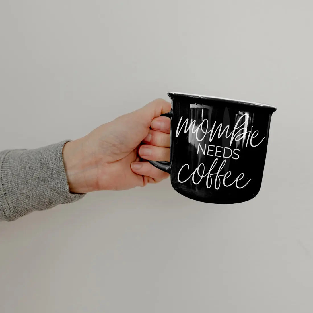 Hand holding a black mug with 'Mommy Needs Coffee' text on a plain background