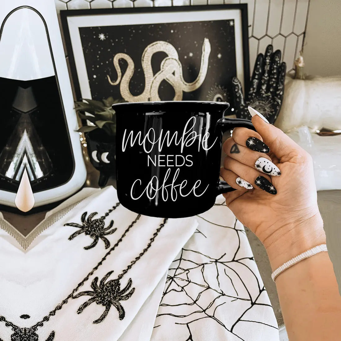 Person holding a black mug with 'mommy needs coffee' text in a Halloween-themed room.