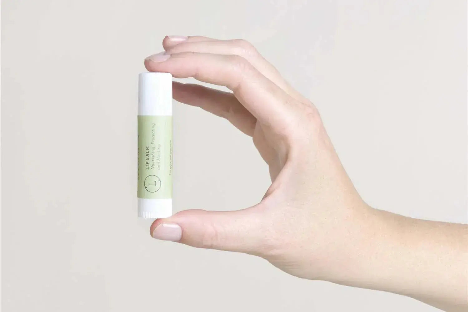 Hand holding nourishing lip balm in minimalist green and white tube, ideal for cozy home self-care routines.