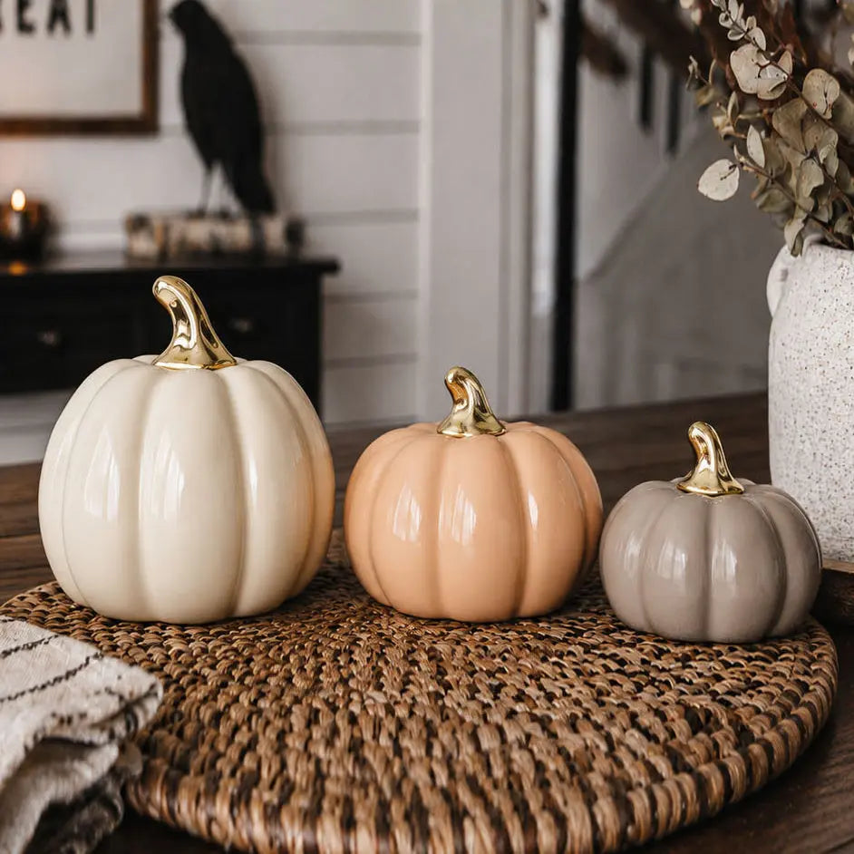 Three decorative pumpkins with gold stems on a woven mat in a home setting.