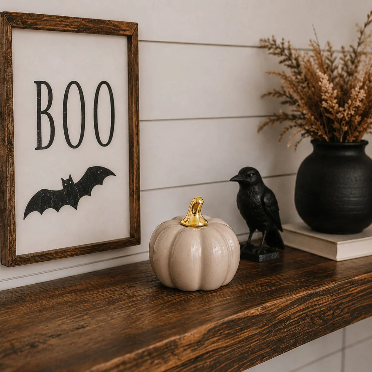 Halloween-themed decor with 'BOO' sign, pumpkin, and crow on a wooden shelf.