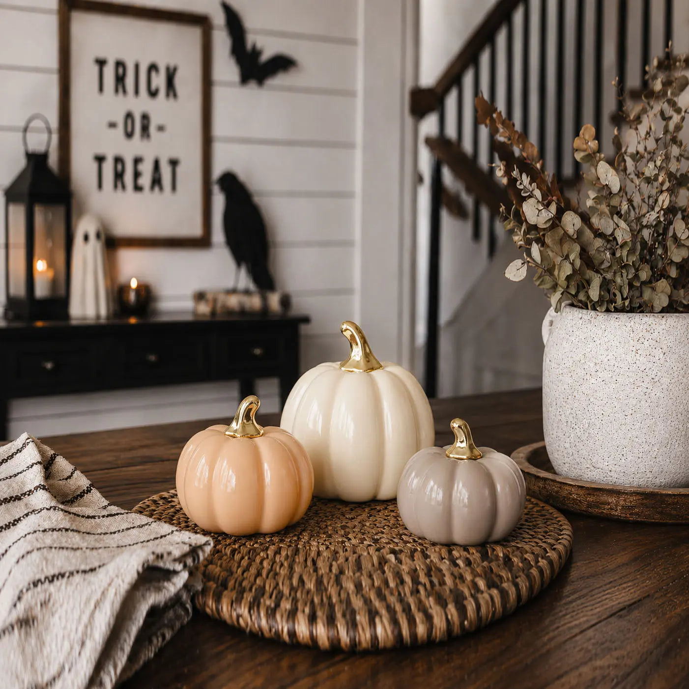 Decorative pumpkins on a woven mat with Halloween-themed decor in the background.