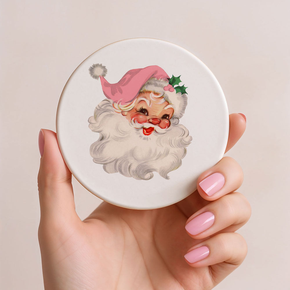 Hand holding a round compact mirror with a Santa Claus design on a beige background