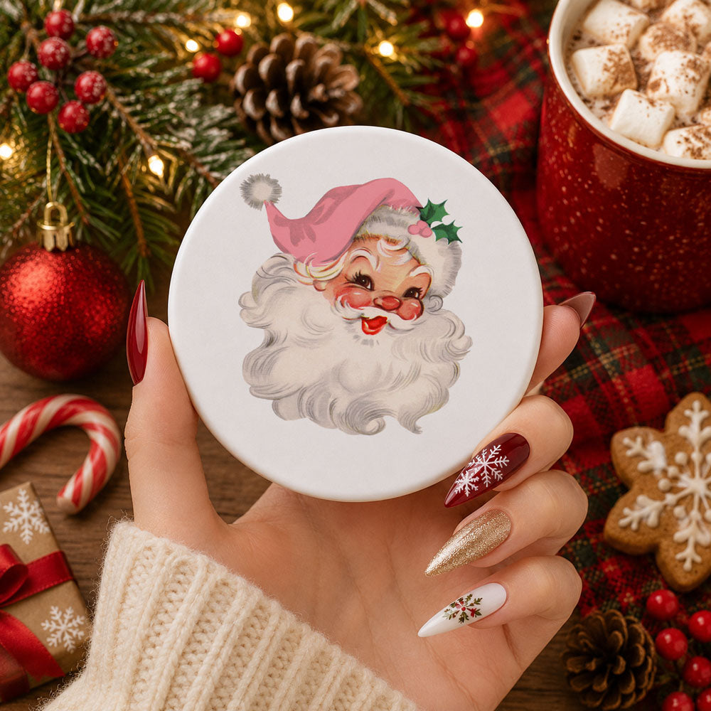 Hand holding a round object with a Santa Claus design, surrounded by Christmas decorations.