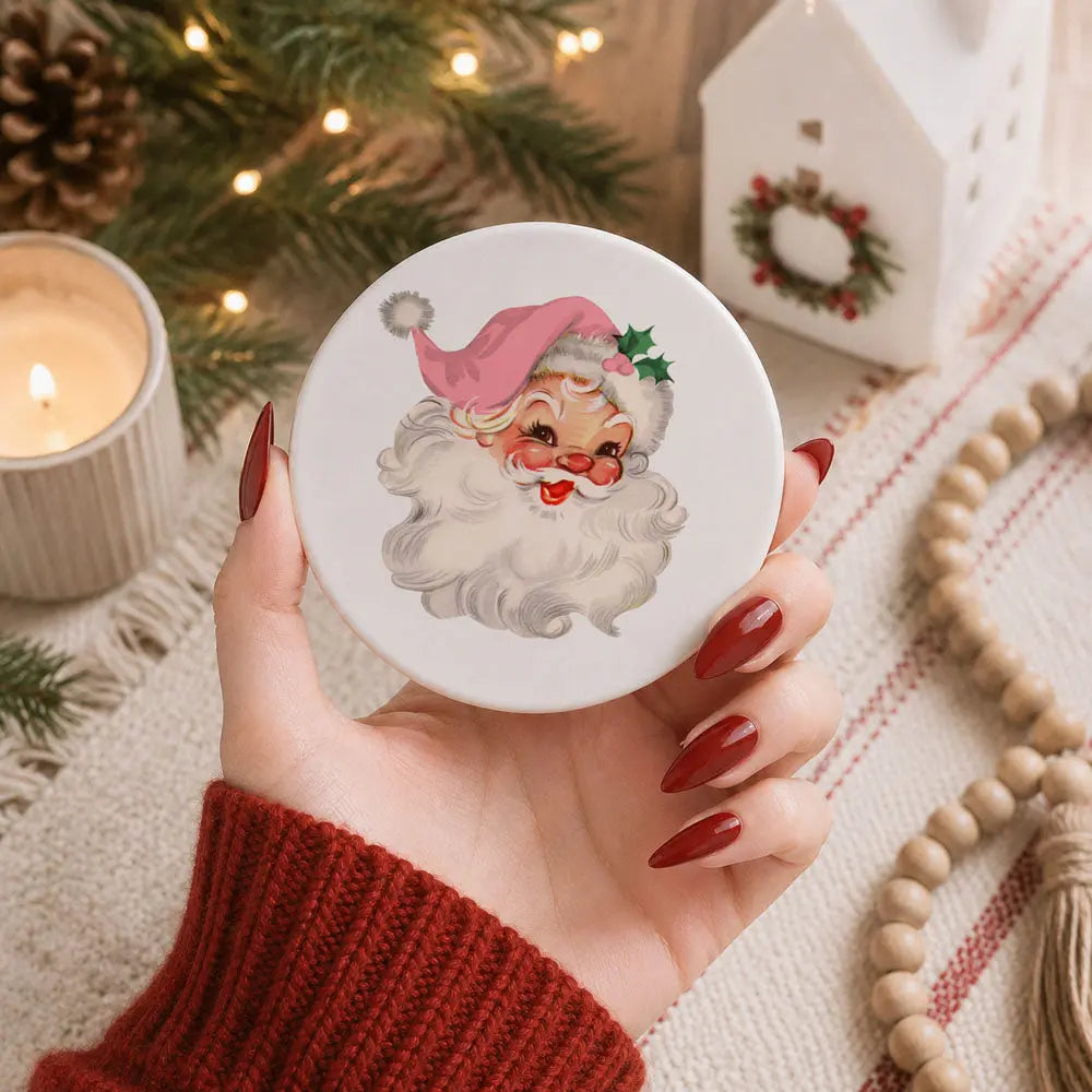 Hand holding a round object with Santa Claus illustration against a festive background with lights and decorations.