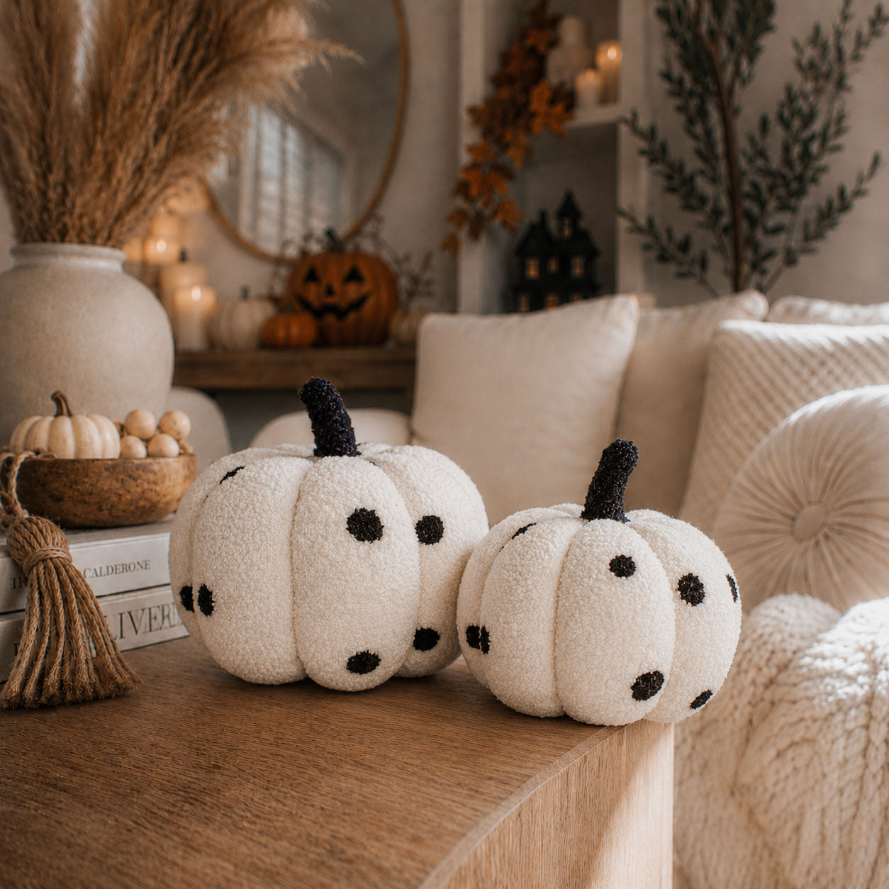 Decorative white pumpkins with black spots on a wooden surface, surrounded by autumn-themed decor.