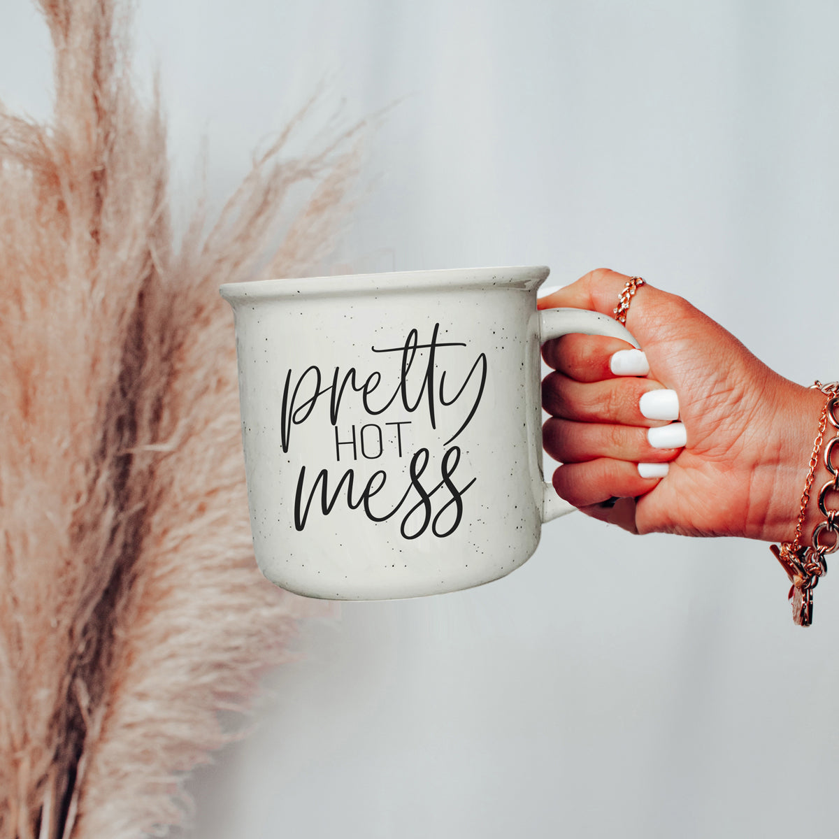 Hand holding a mug with 'pretty hot mess' text against a neutral background