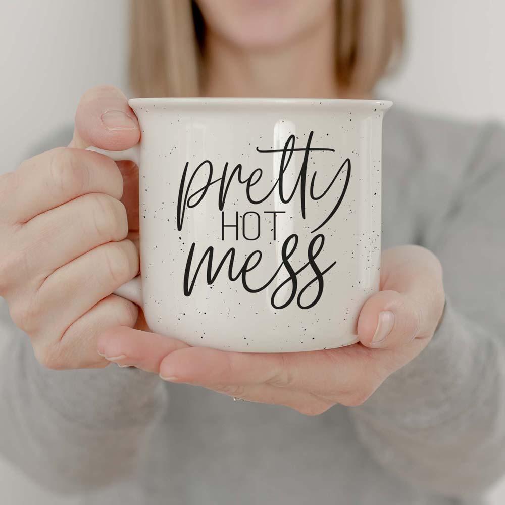 Person holding a mug with 'pretty hot mess' text
