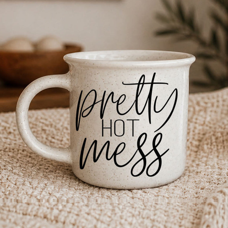 White mug with 'pretty hot mess' text on a textured surface
