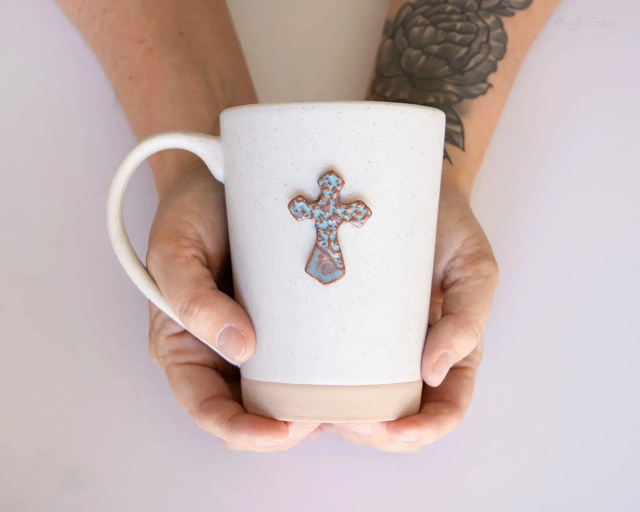 White speckled ceramic mug with blue and copper cross, held in hands, farmhouse style home decor