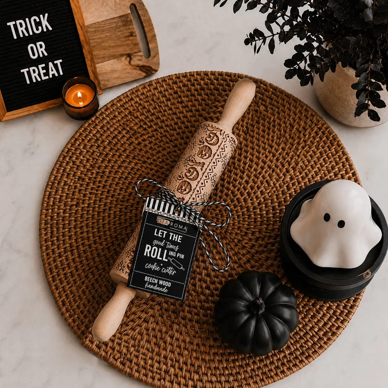Wooden rolling pin with decorative patterns on a woven mat, surrounded by Halloween-themed items.