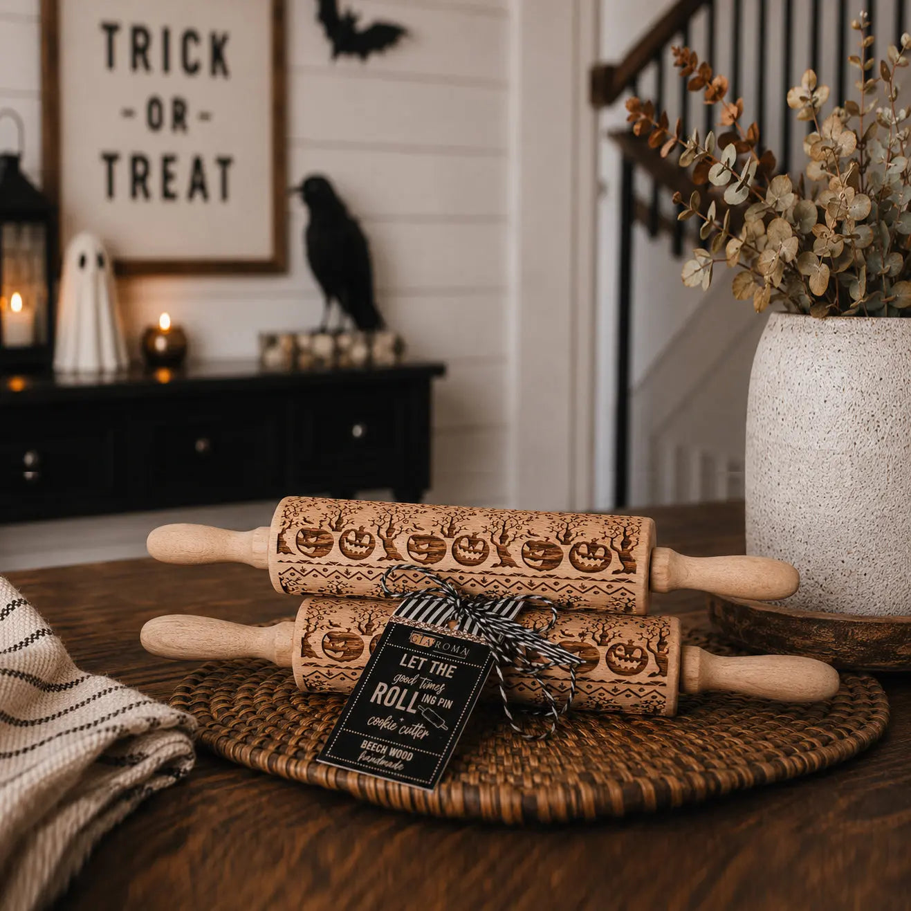 Two wooden rolling pins with Halloween designs on a wooden surface, with a 'Trick or Treat' sign and decorative items in the background.