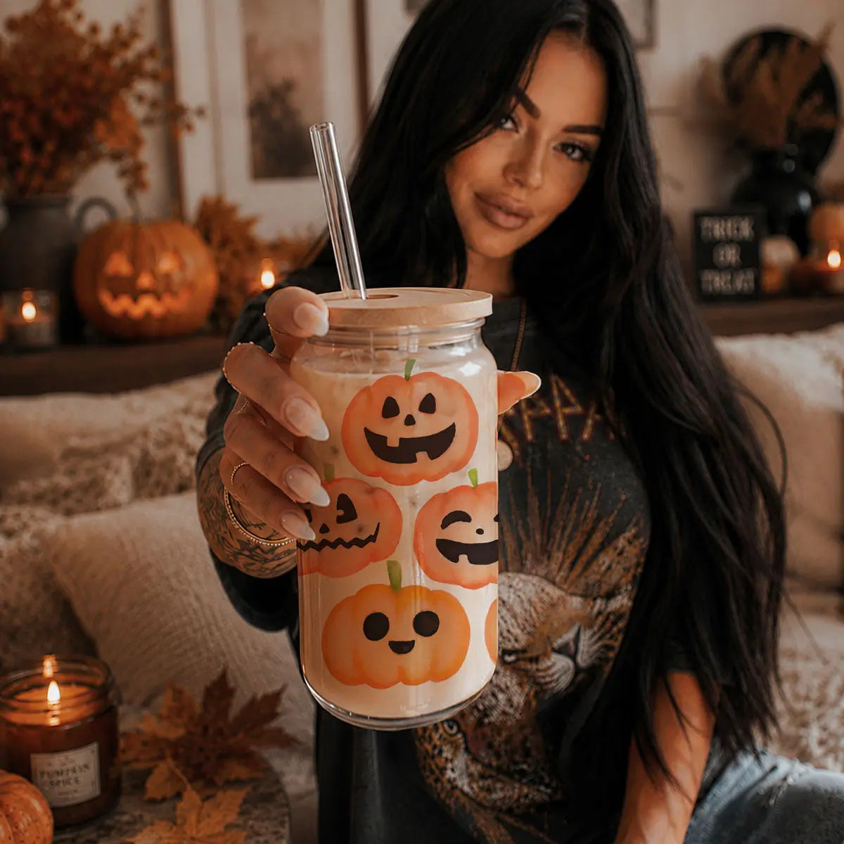 Woman holding a Halloween-themed cup with pumpkins in a cozy indoor setting.