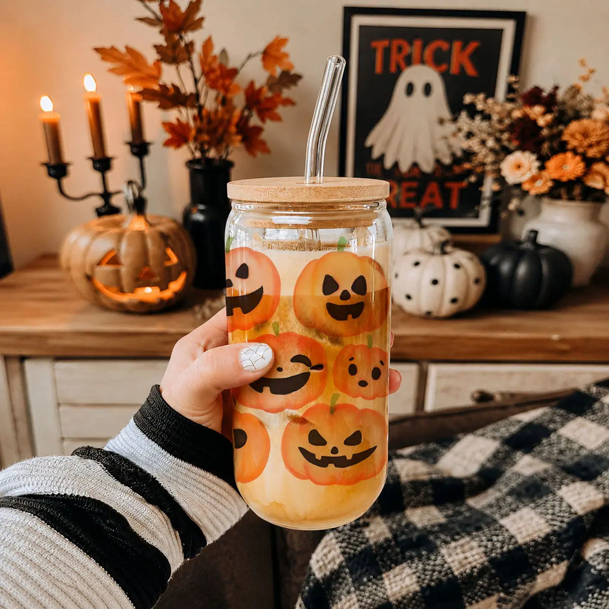 Person holding a Halloween-themed glass with pumpkins, decorated with fall decor in the background.