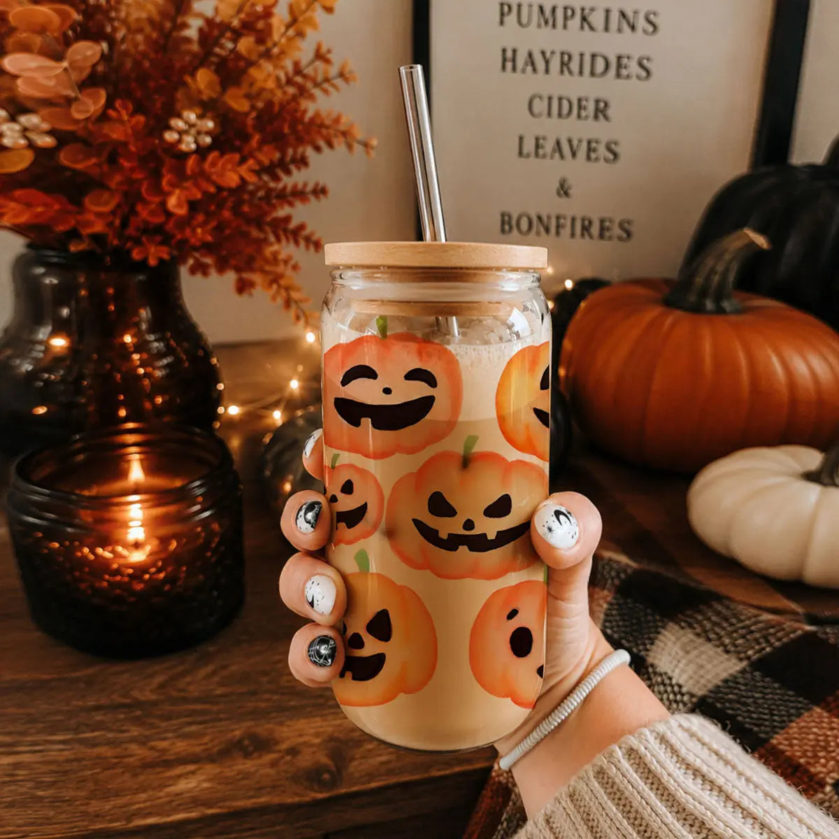 Hand holding a glass tumbler with Halloween-themed design in a cozy autumn setting.