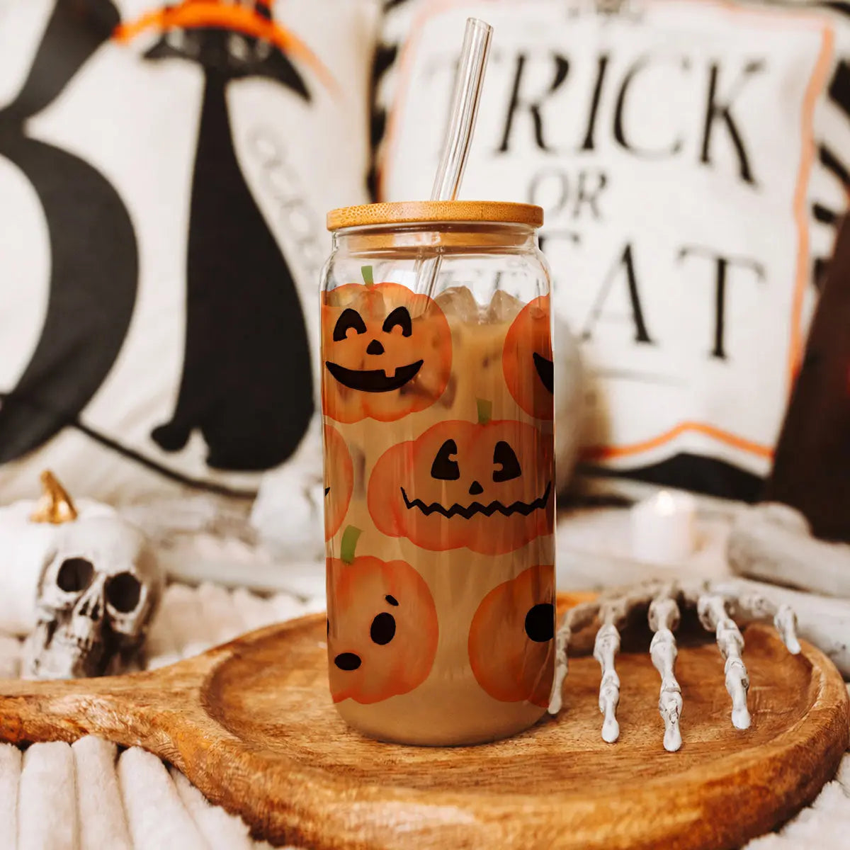 Glass tumbler with Halloween-themed design on a wooden coaster, surrounded by festive decorations.