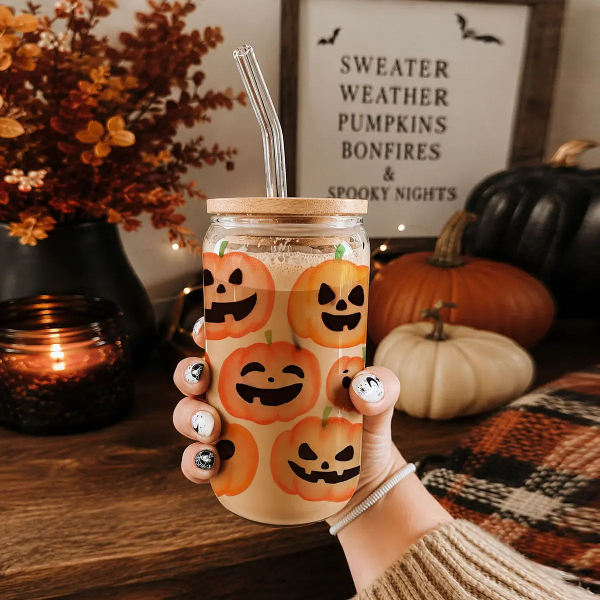 Hand holding a jar with Halloween-themed pumpkins design, surrounded by autumn decor.