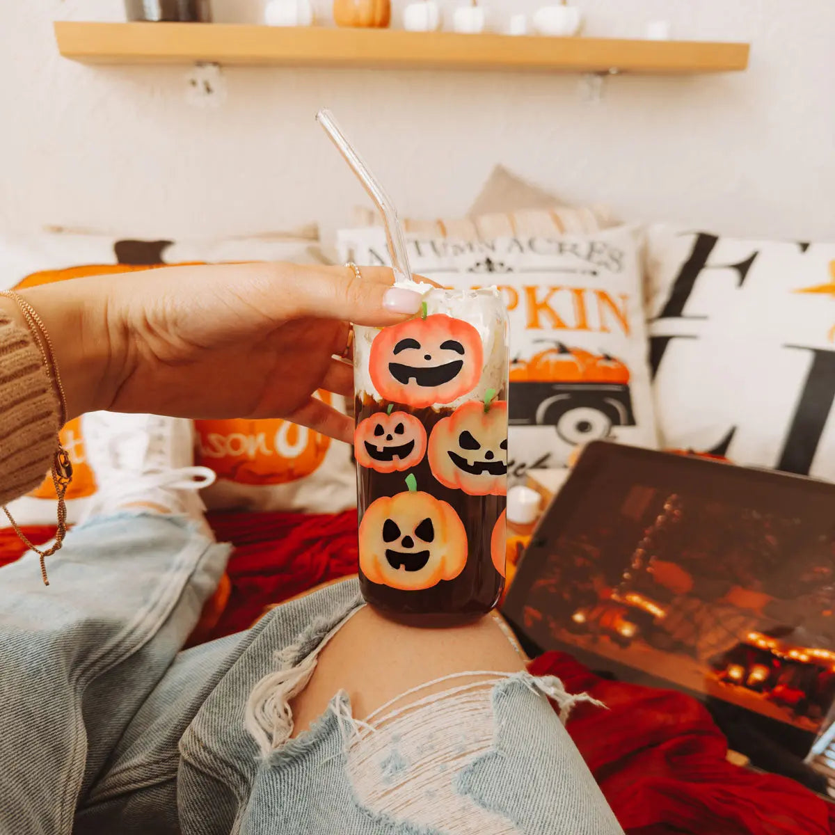Person holding a Halloween-themed drink with pumpkins in a cozy indoor setting.