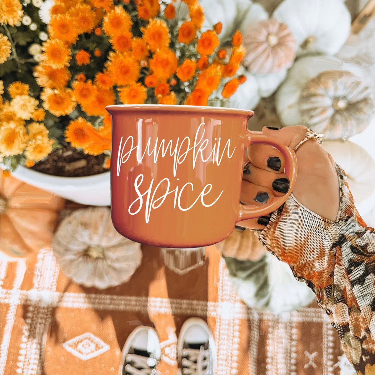 Orange 'Pumpkin Spice' mug held by a hand with plaid sleeve, surrounded by autumn decorations.